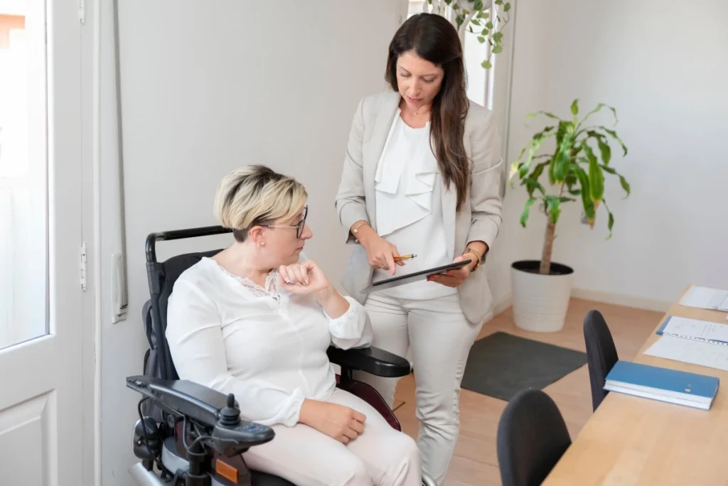 A disabled woman sitting in her wheelchair and her support worker looking at an iPad together