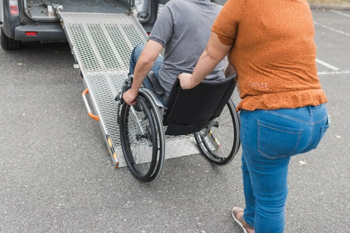A disabled man sitting in his wheelchair and his support worker assisting him in the car via the ramp